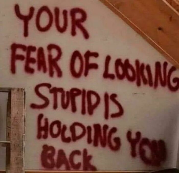 Graffiti vandalized public property with a motivational message spray painted in red on a white wall under a wooden ceiling.