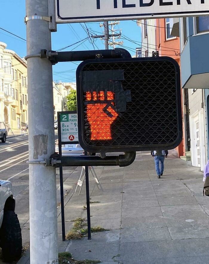 Pedestrian signal creatively vandalized to show a raised fist instead of the usual stop hand on a city sidewalk.