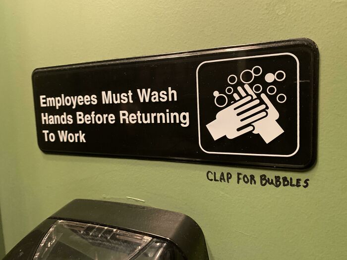 Sign instructing employees to wash hands with added vandalism text saying clap for bubbles on a public property wall.