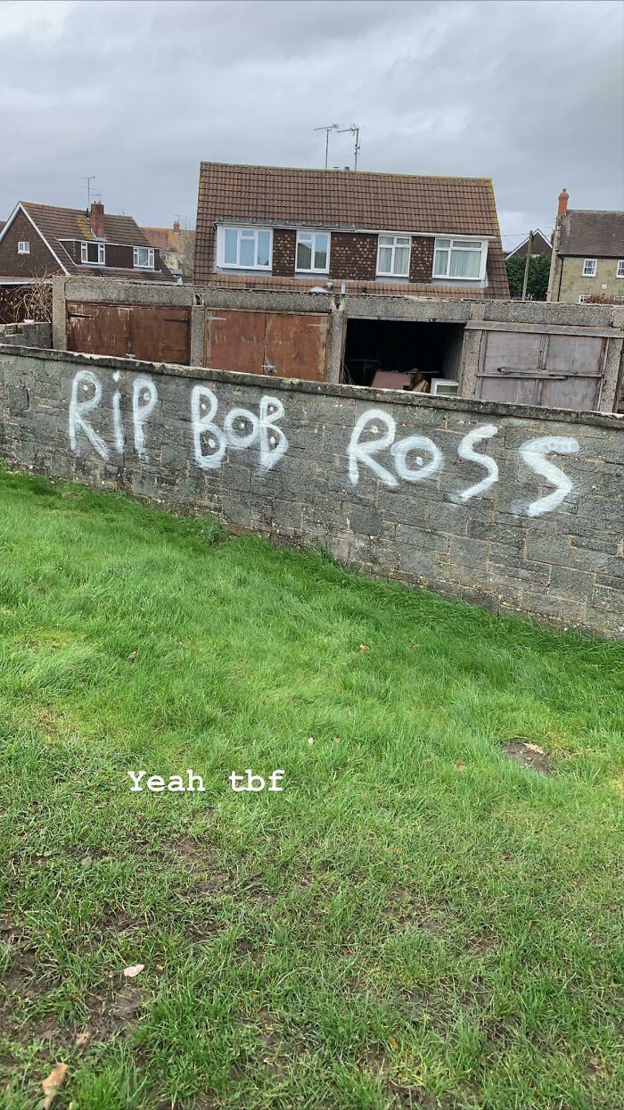 Graffiti vandalism on a stone wall with a tribute message to Bob Ross in a residential neighborhood.