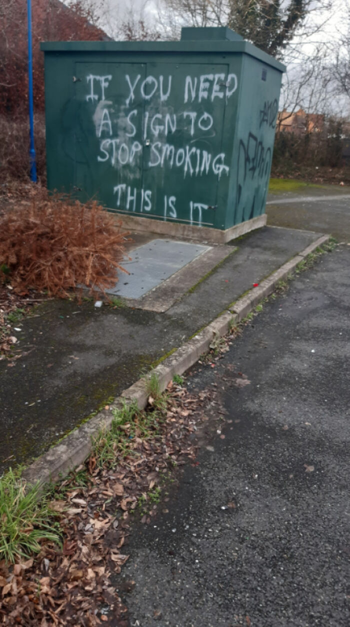 Graffiti vandalism on public property with a clever anti-smoking message sprayed on a green utility box outdoors.