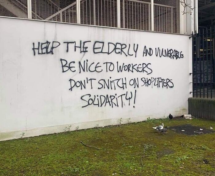 Graffiti on white wall promoting kindness, solidarity, and support for elderly and workers as creative vandalized public property.