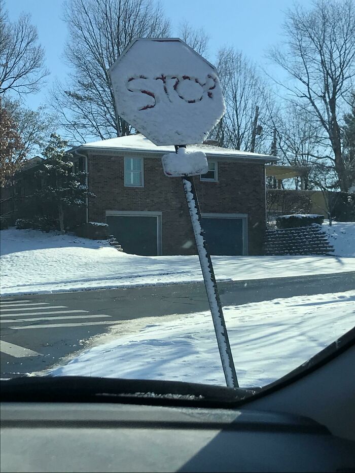 Snow-covered stop sign vandalized by scraping letters, showcasing creative public property vandalism in a snowy suburban neighborhood.