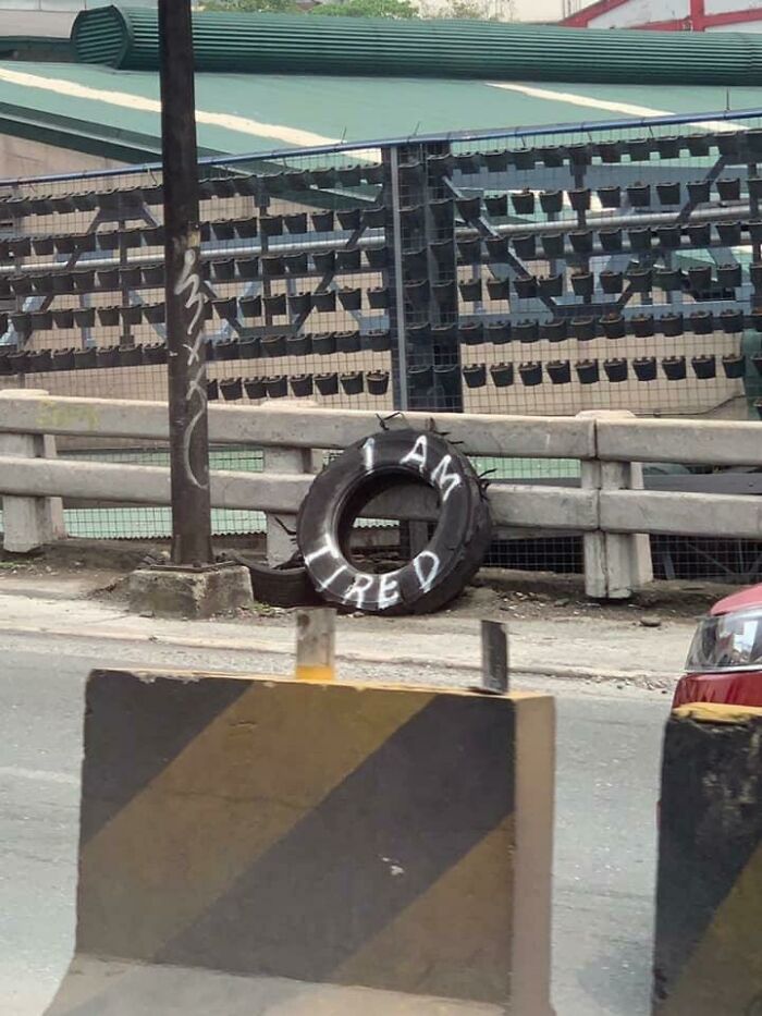 Tire with graffiti saying I am tired leaned against a fence, a creative example of people vandalizing public property.