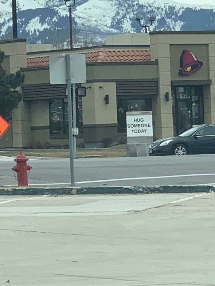 A public property sign altered to read Hug Someone Today in front of a restaurant with mountains in the background.