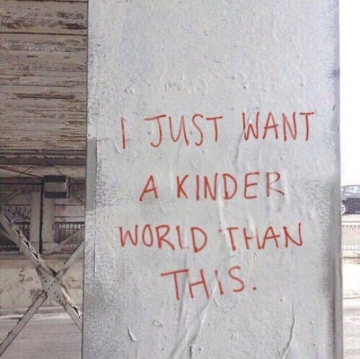 Graffiti vandalism on public property expressing a desire for a kinder world with red handwritten text on a white wall.