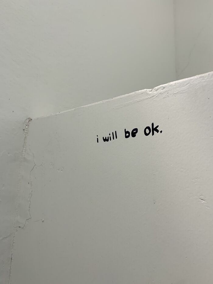 Minimalist vandalized public property with a hopeful message saying i will be ok written in black on a white wall.