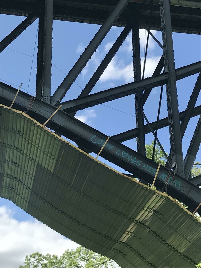Graffiti vandalized on a public bridge beam with love message visible under blue sky and metal structure.