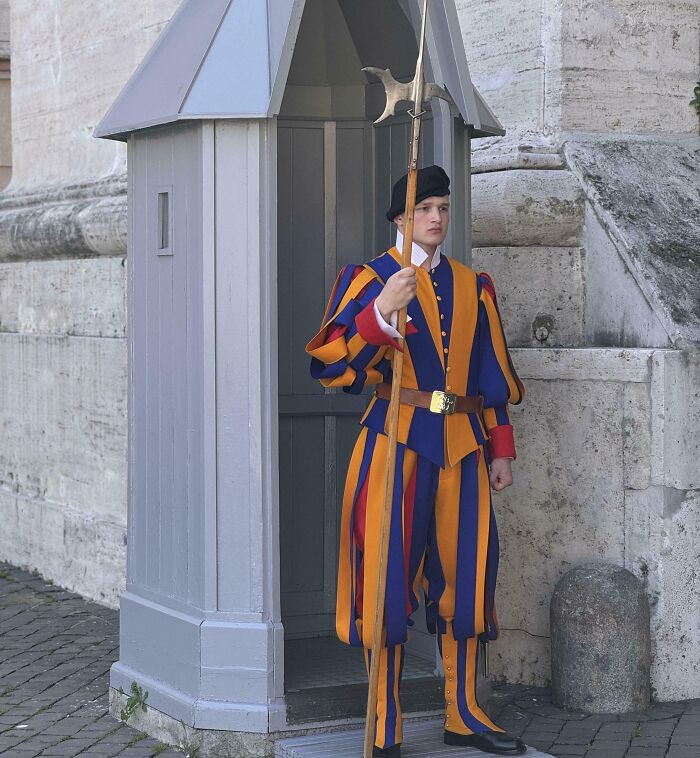 Swiss Guard in colorful uniform standing at guard post holding a polearm, showcasing unique wearing a uniform style.
