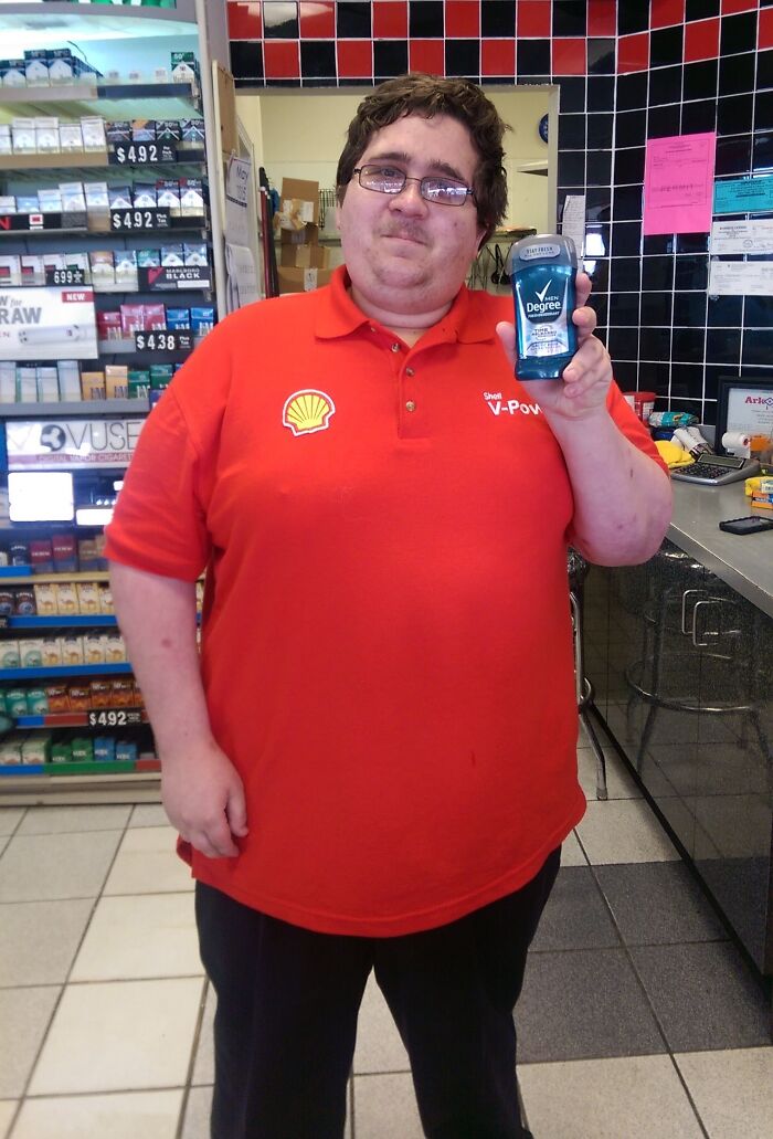 Man wearing a Shell uniform holding deodorant in a store, showcasing a funny moment of wearing a uniform.
