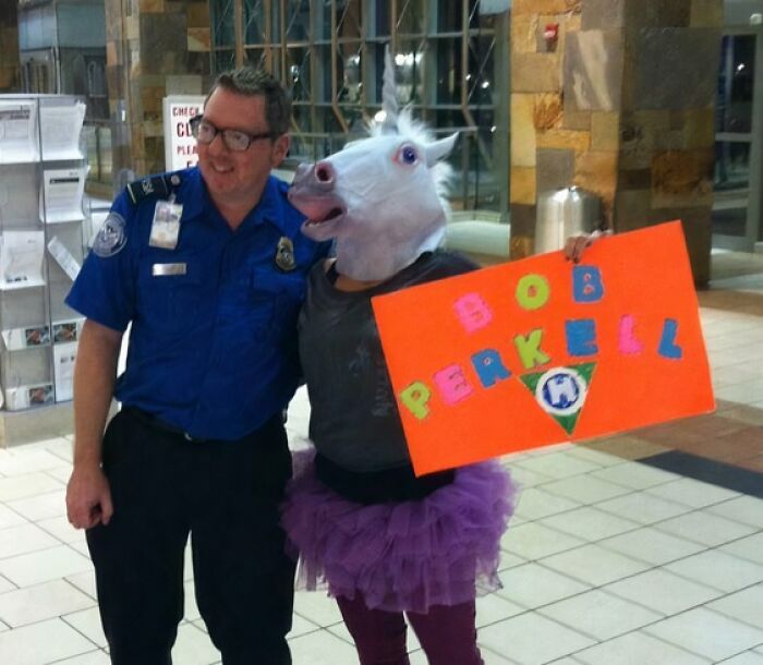 Security officer smiling beside person wearing horse mask and tutu holding colorful sign, showing funny uniform moments.