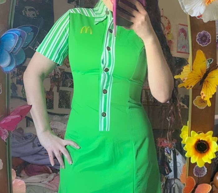 Person wearing a bright green McDonald's uniform dress with mismatched stripes and buttons, posing in a decorated room.
