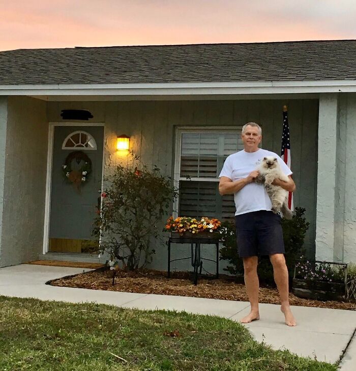 Man standing barefoot in front of house holding cat, illustrating dads who said no pets and became softies.