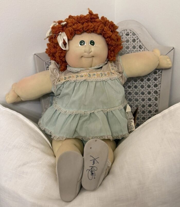 Vintage toys worth fortune featuring a collectible doll with red curly hair and a blue dress sitting on a chair.