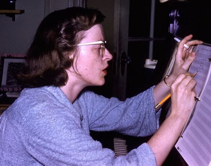 Woman with glasses in a cozy sweater writing music notes with a pencil, related to celebrities who vanished without a trace.