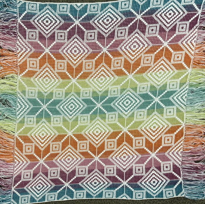 Crocheted colorful geometric pattern blanket with fringe, showcasing detailed craftsmanship and mastering the art of crocheting.