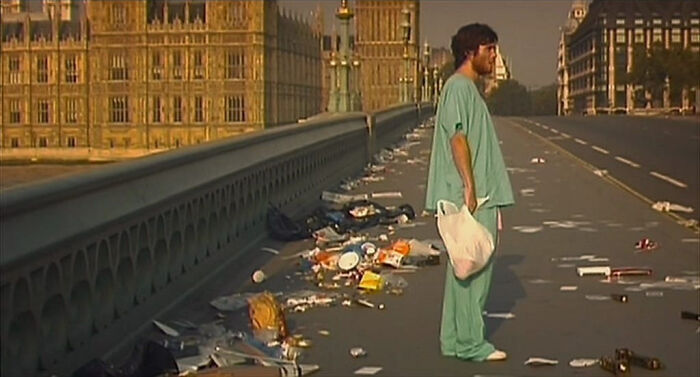 Man in green scrubs stands on empty littered bridge in confusing bad movie scene from an online group dedicated to bad movie details.