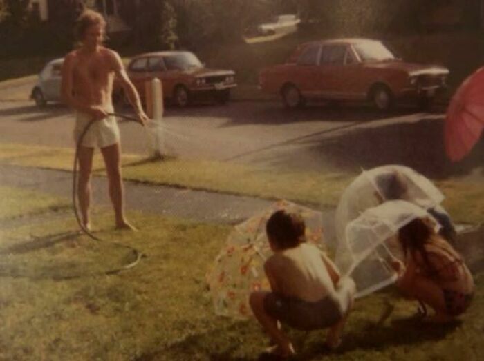 Vintage outdoor scene with children playing with umbrellas and a man spraying water, capturing a moment of terrifying photos.