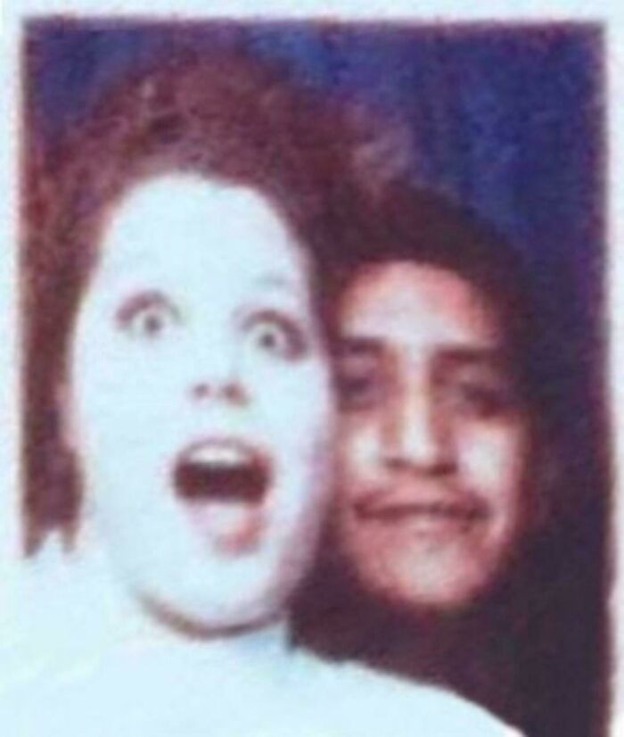 Terrifying photo of a woman with a shocked expression and a mysterious figure behind her in a dark setting.