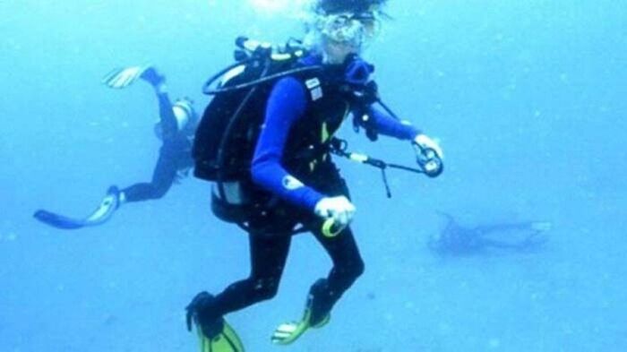 Scuba divers underwater with a shark approaching in the background in a terrifying and scary ocean scene.