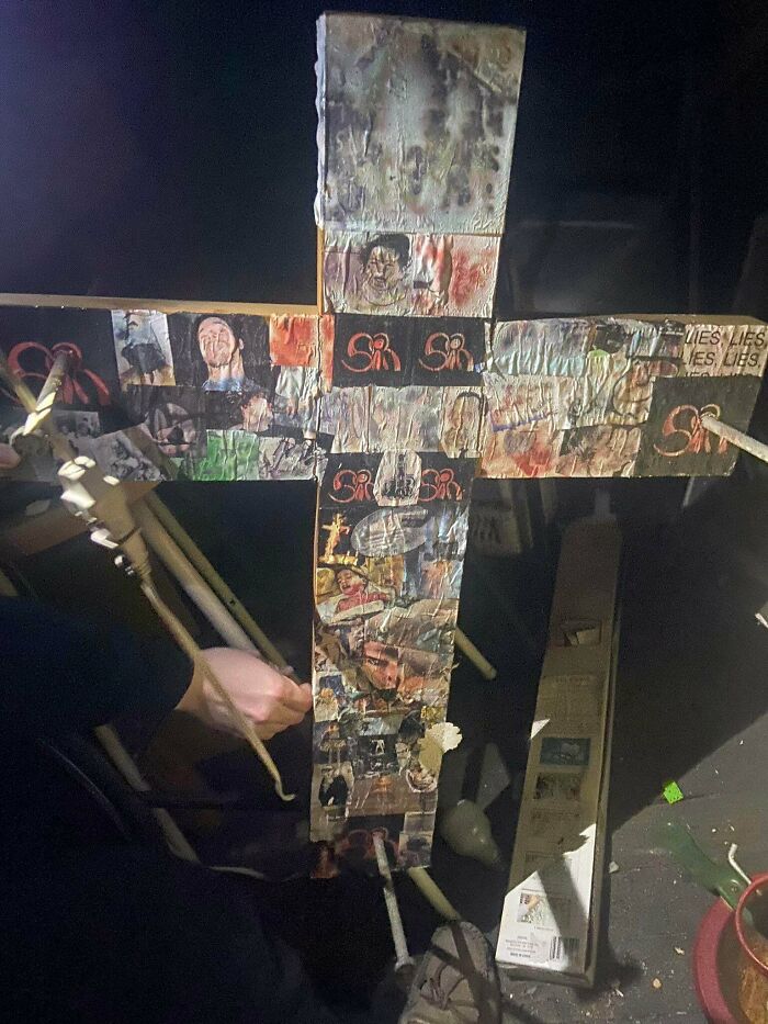 Hand holding a dark cross covered in disturbing images and text, capturing terrifying photos and stories.