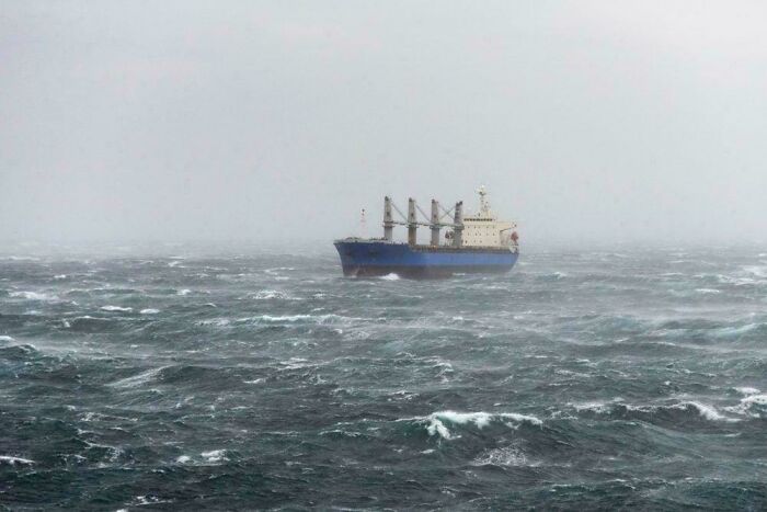 Large cargo ship navigating rough, stormy ocean waters during a cold, foggy and terrifying sea storm scene.