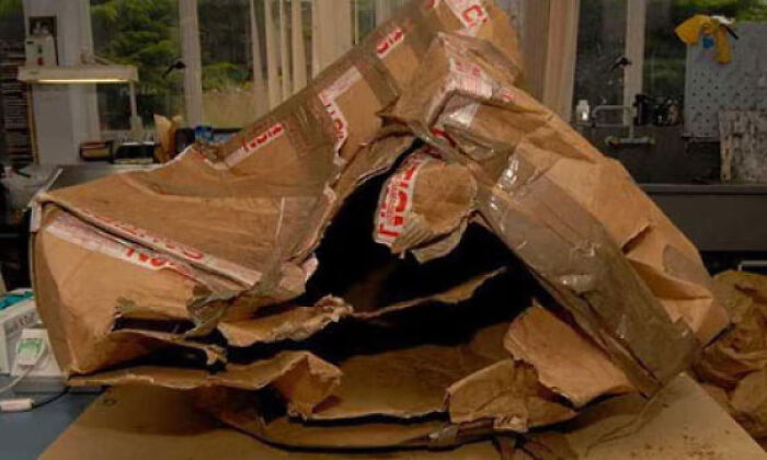Large torn and crushed cardboard box on a table, evoking eerie and terrifying photos with mysterious elements indoors.