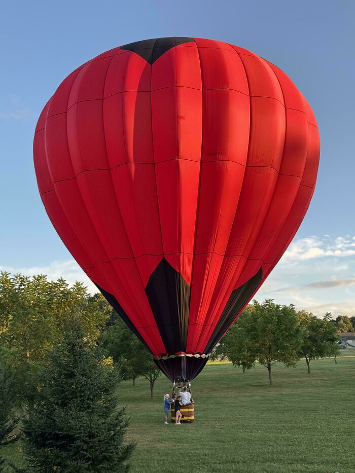 Red hot air balloon on the ground with people preparing for takeoff, showcasing moderately interesting scenes shared online.