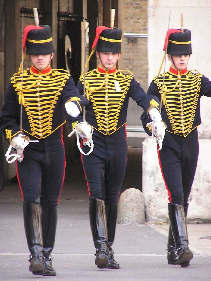 Three men wearing ornate ceremonial military uniforms marching with swords during a formal event.