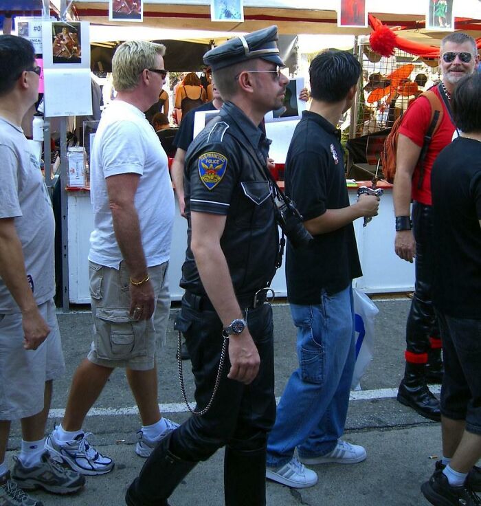 Man in a police uniform walking among casually dressed people at an outdoor event, showcasing funny uniform moments