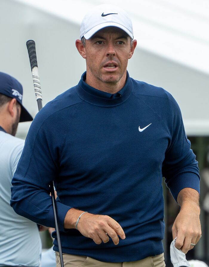Golfer in a navy blue Nike sweater and white cap holding a golf club, featured among highest paid athletes 2025.