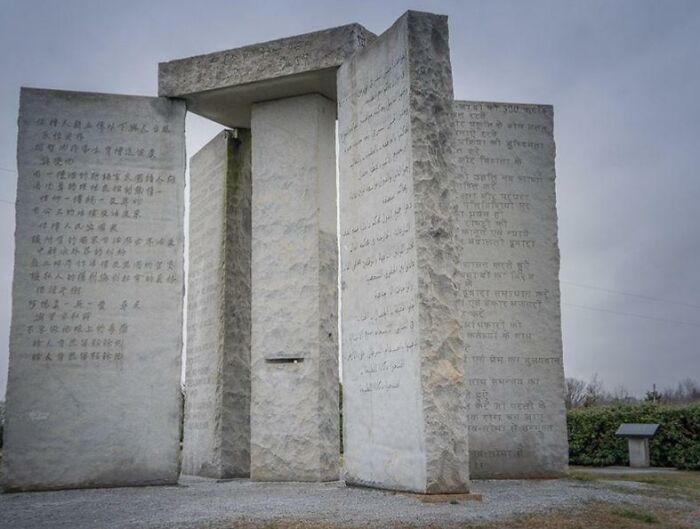 Mysterious stone monument with inscriptions in multiple languages under a cloudy sky, evoking terrifying stories and fascination.