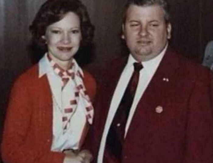 Couple dressed in vintage attire posing formally in a dimly lit room for terrifying photos and stories.