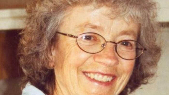 Smiling elderly woman with curly gray hair and glasses in a warm indoor setting, related to terrifying photos and stories.