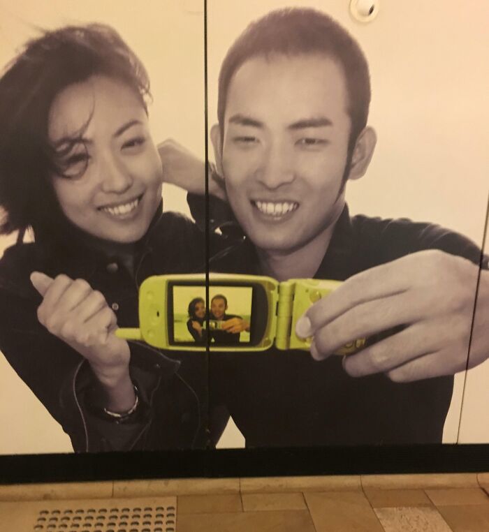 Couple taking a selfie with a yellow flip phone showing a distorted image, highlighting notable Photoshop fails.
