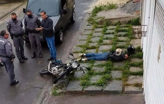 Man lying on the ground next to a fallen motorcycle with chubby round funny cats sitting on his back near police officers.