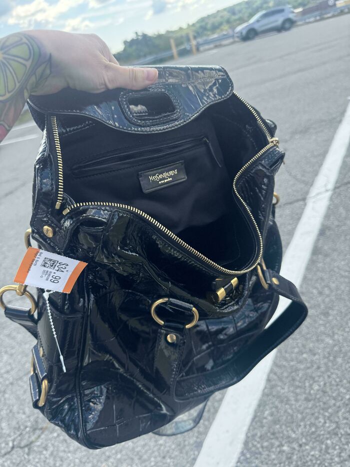 Black Yves Saint Laurent purse found at thrift store with price tag held open outdoors in a parking lot.