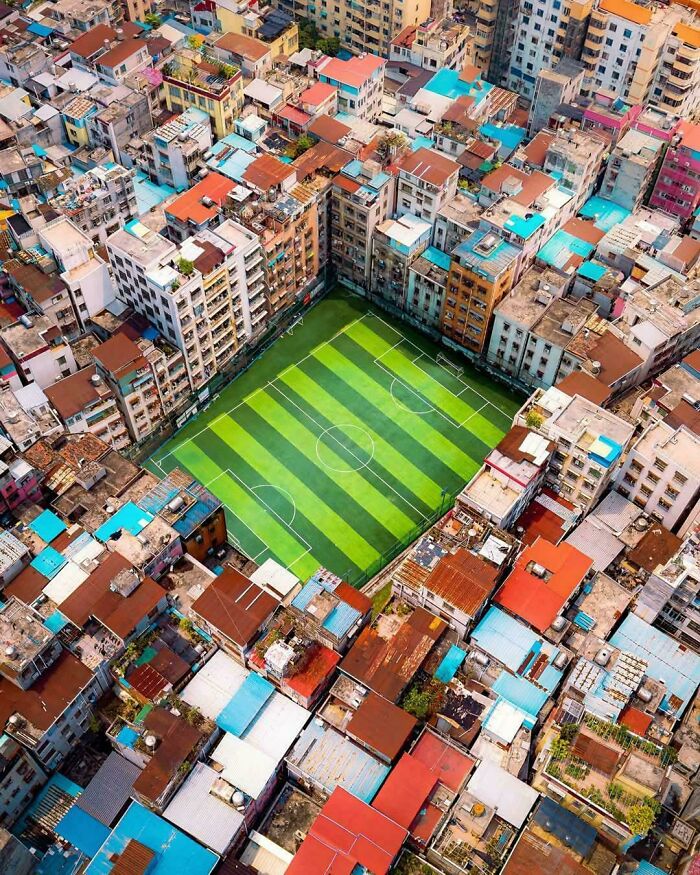 Aerial view of a cramped urban area with densely packed buildings surrounding a small green soccer field.