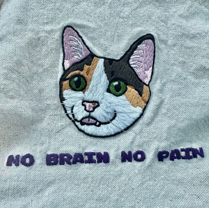 Fun embroidery creations of a calico cat head with green eyes and the text NO BRAIN NO PAIN, a quirky hobby.