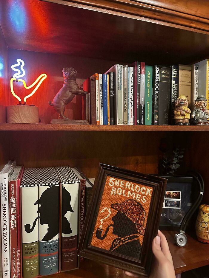 Thrift store finds featuring Sherlock Holmes books, figurines, and neon pipe light on a wooden bookshelf.