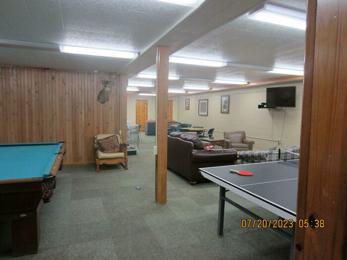 Dimly lit break room with dated furniture and games, giving a prison-like and uncomfortable atmosphere.