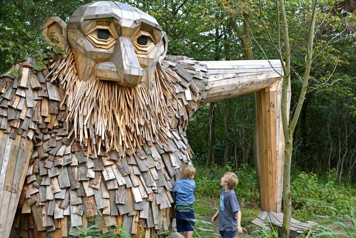 Wooden troll sculpture in a forest, with two children exploring, showcasing unique Danish art and culture.