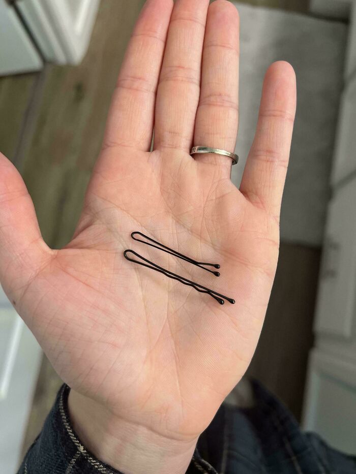 Close-up of a hand holding two black bobby pins, illustrating everyday things that humble fully grown adults.