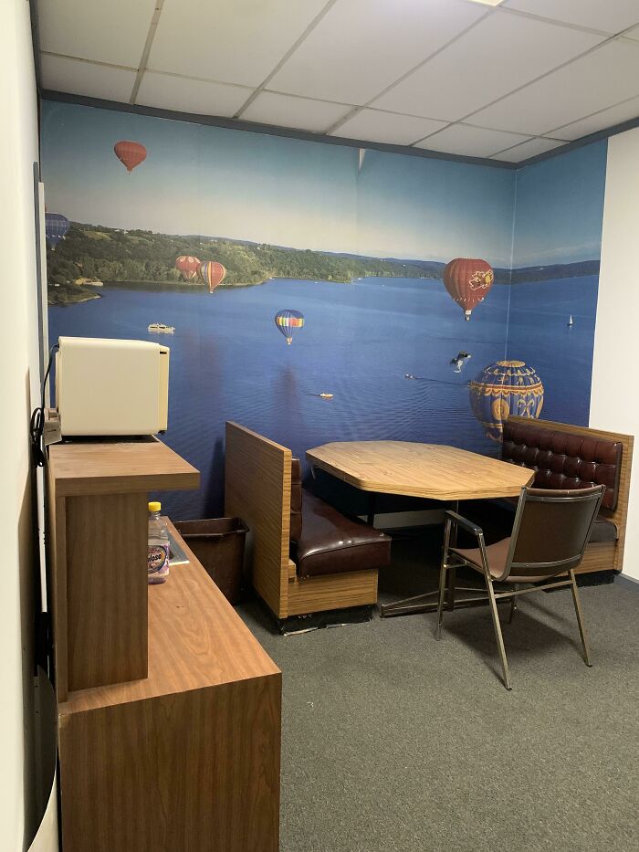 Small break room with dated furniture and a mural, illustrating one of the worst break rooms ever design.