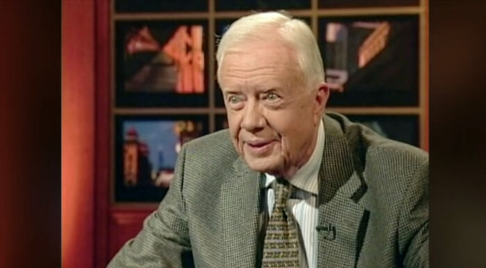 Elderly man in a gray suit and patterned tie speaking in a studio setting, representing time perception comparisons.