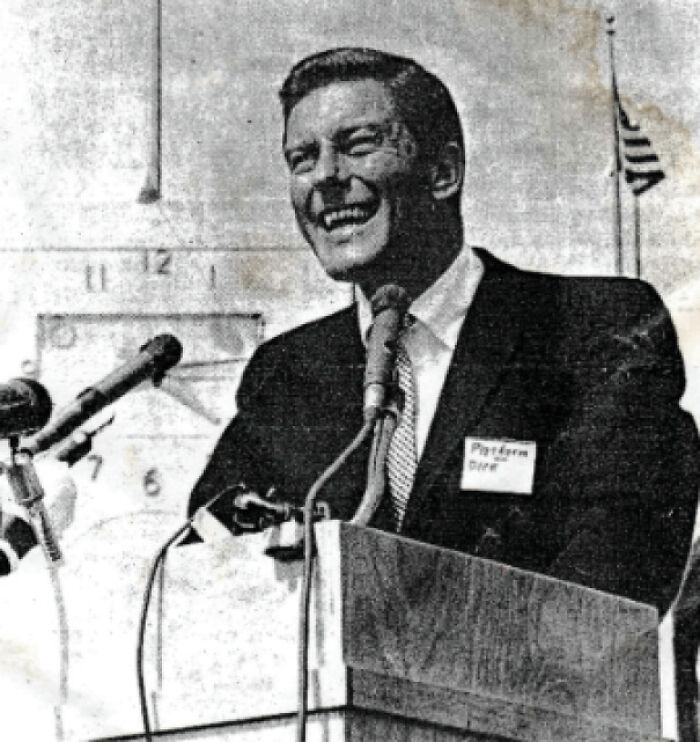 Man in a suit speaking at a podium with microphones, black and white photo highlighting perception of time concept.