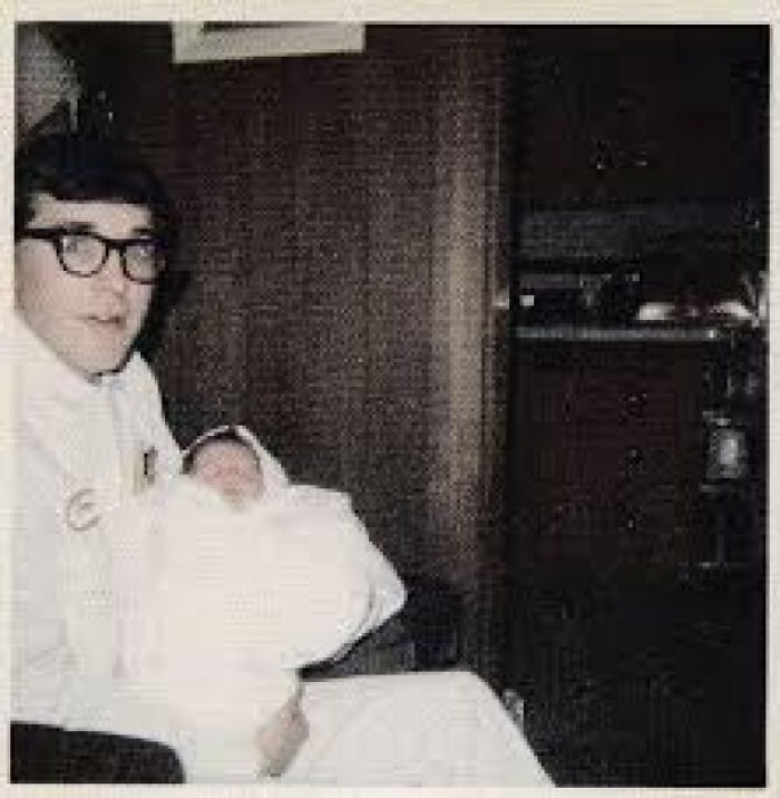 Man in glasses holding a newborn baby indoors, illustrating random comparisons that mess with perception of time.