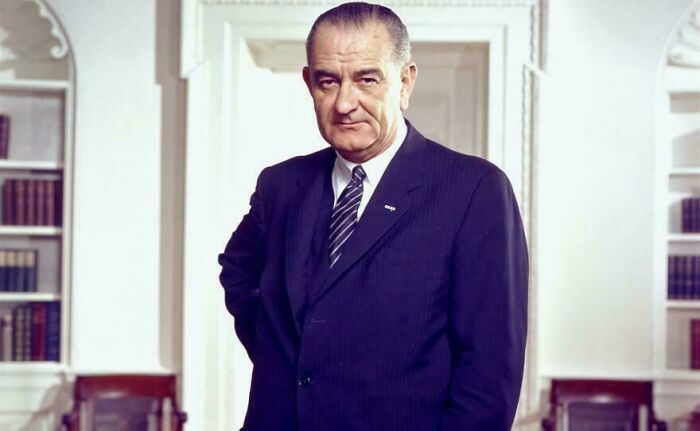 Portrait of a man in a suit standing indoors, related to online group sharing random comparisons about perception of time.