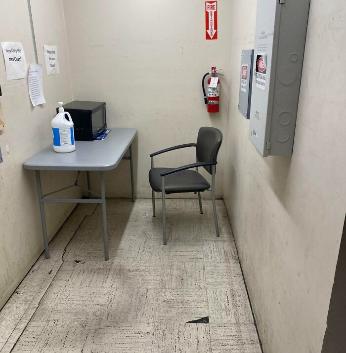 Bare, prison-like break room with plastic chair, microwave on small table, and fire extinguisher on stained walls.