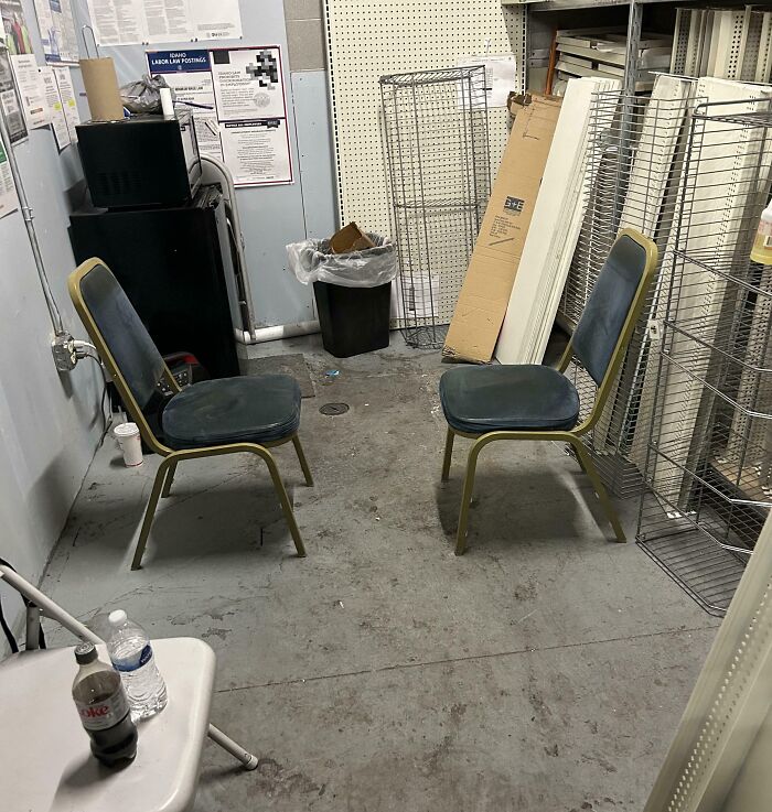Small cluttered break room with worn chairs, trash can, and storage racks, resembling one of the worst break rooms ever.